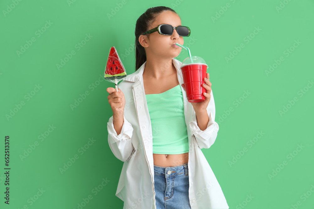 Little girl with lollipop in shape of watermelon slice and soda on green background