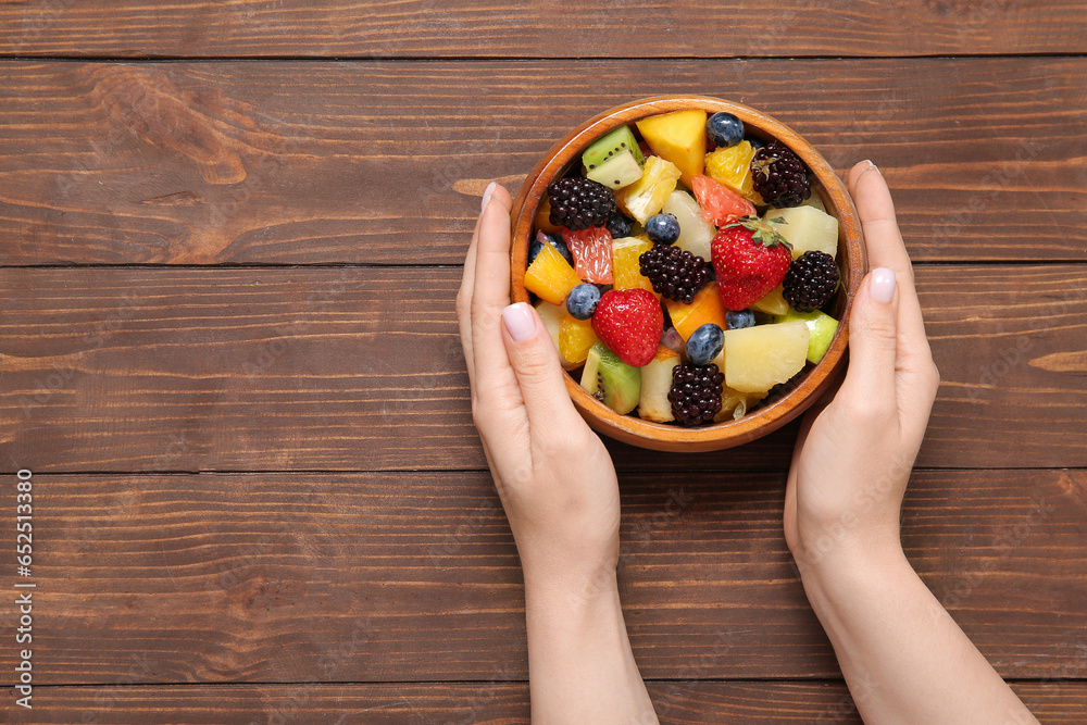 Woman with bowl of fresh fruit salad on wooden background