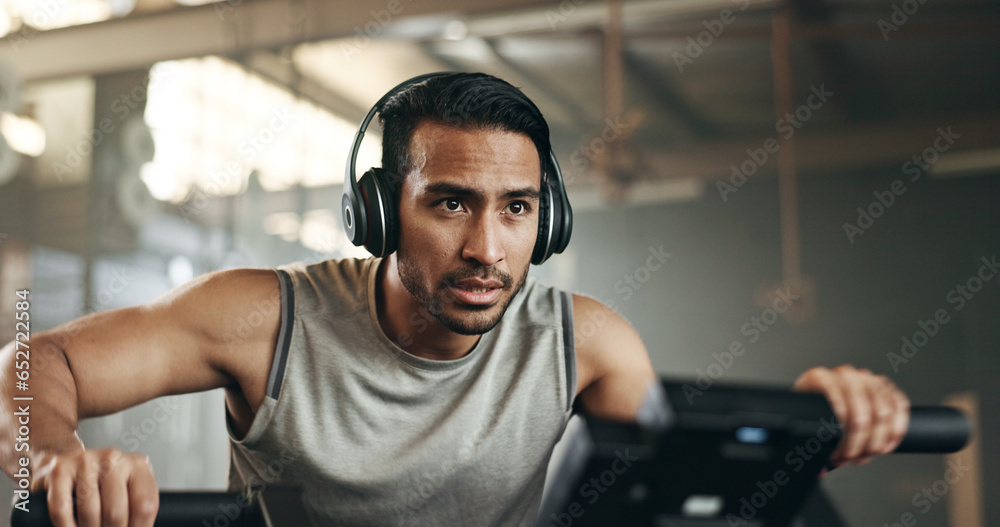 Asian man, headphones and cycling at gym on machine and listening to music in sports workout or exercise. Serious male person or athlete training on bicycle machine or equipment for healthy cardio