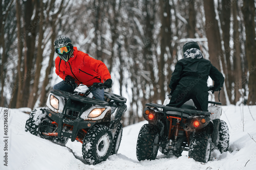 Riding the opposite ways. Two people are on the ATV in the winter forest