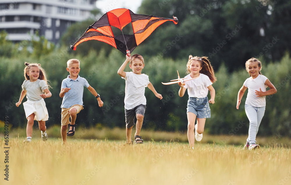 Running together. Group of kids are running and playing with kite on green field