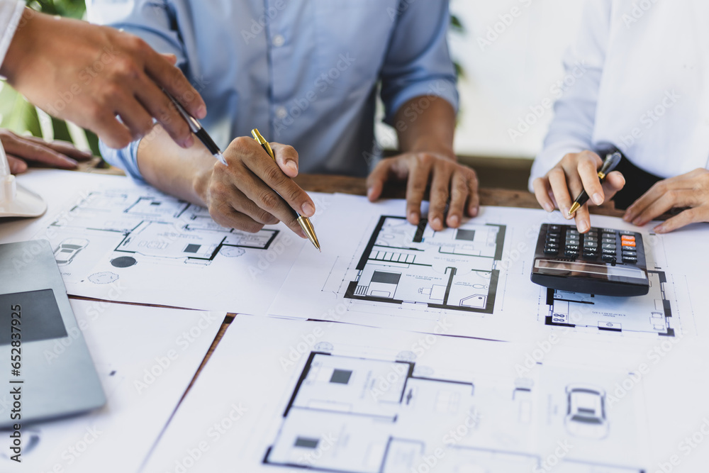 Brainstorming group of architects and engineers discuss building blueprint design and construction project planning on wooden table in office.