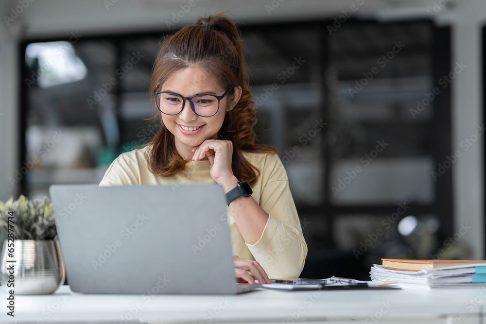 Asian businesswoman or accountant using laptop computer to explain online meeting or online training, paperwork, accounting, marketing, finance on office desk.