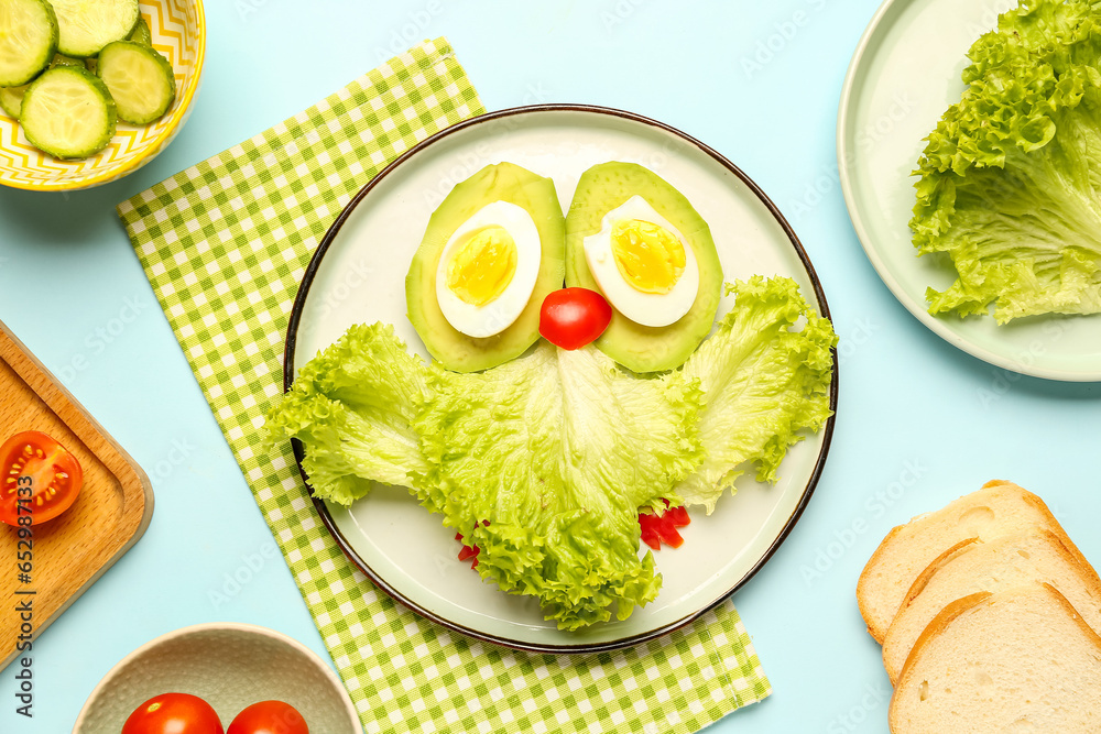 Plate with funny breakfast in shape of owl, vegetables and bread on blue background