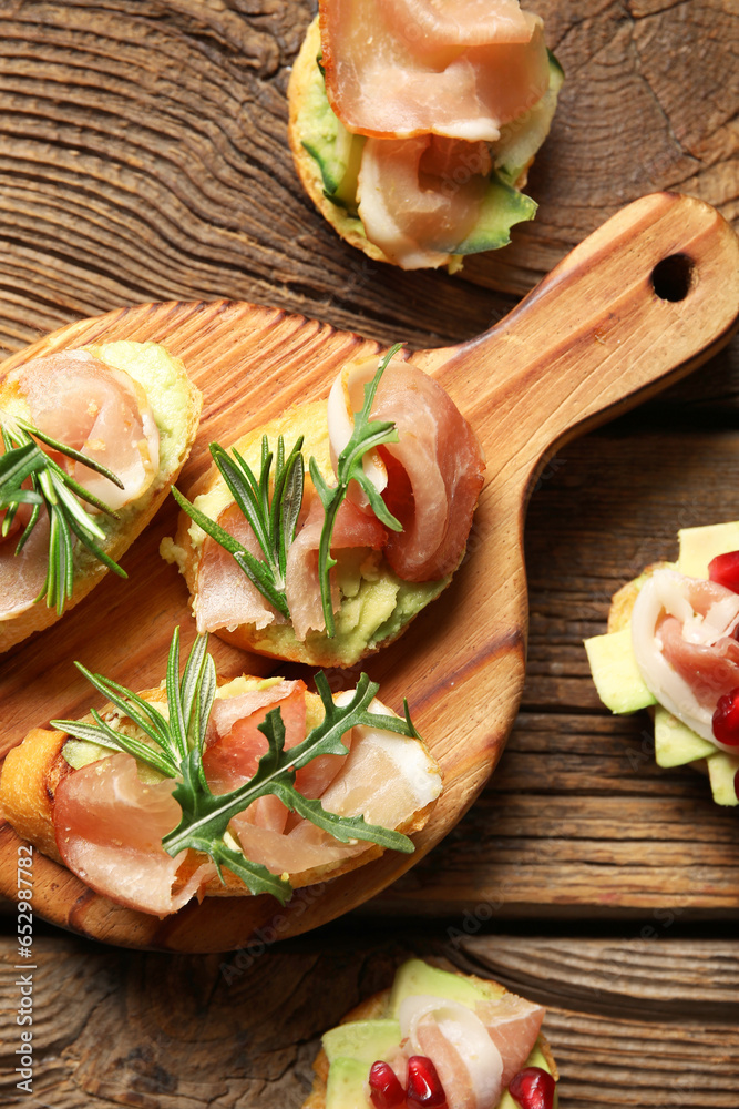 Board of tasty bruschettas with ham on wooden background