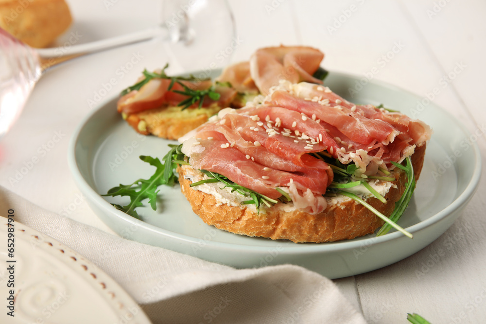 Plate of tasty bruschettas with ham on white wooden background