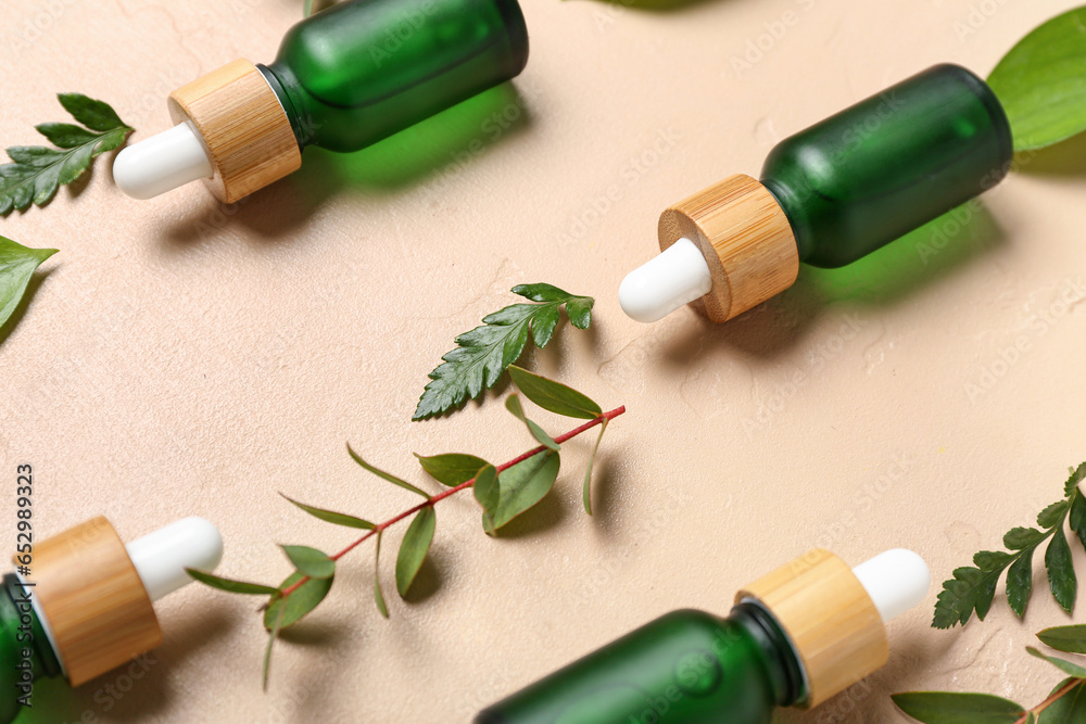 Bottles of cosmetic oil with plant twigs on beige background