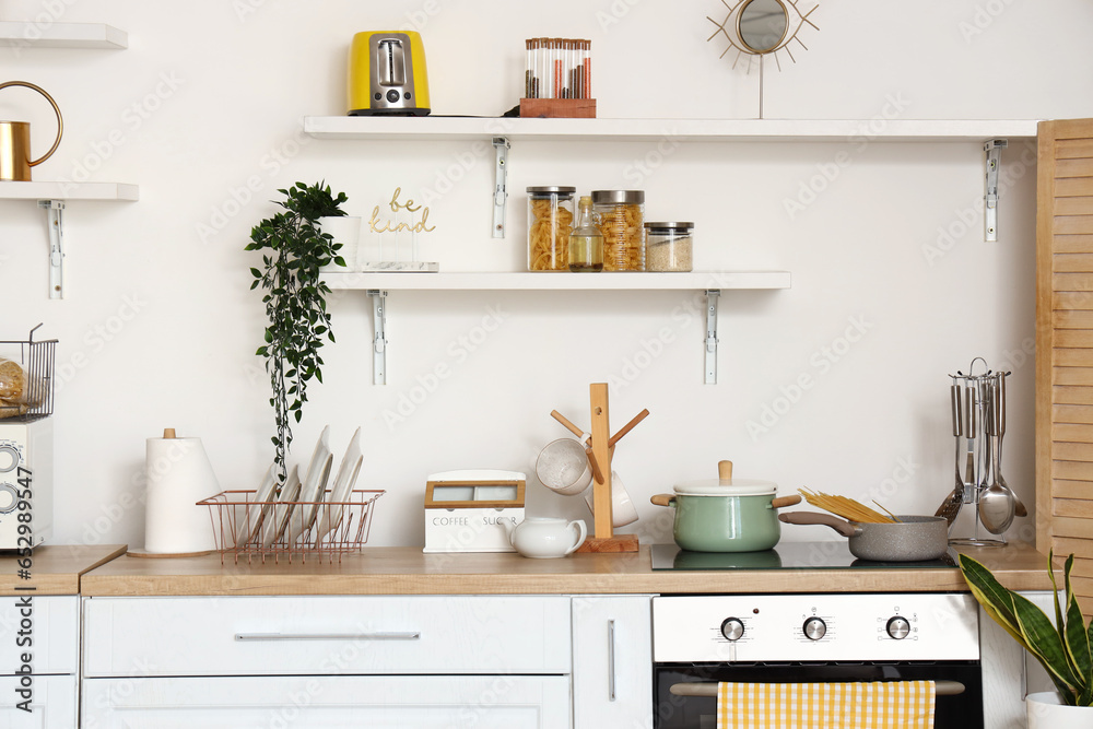 Interior of light kitchen with stylish counters, electric oven and shelves