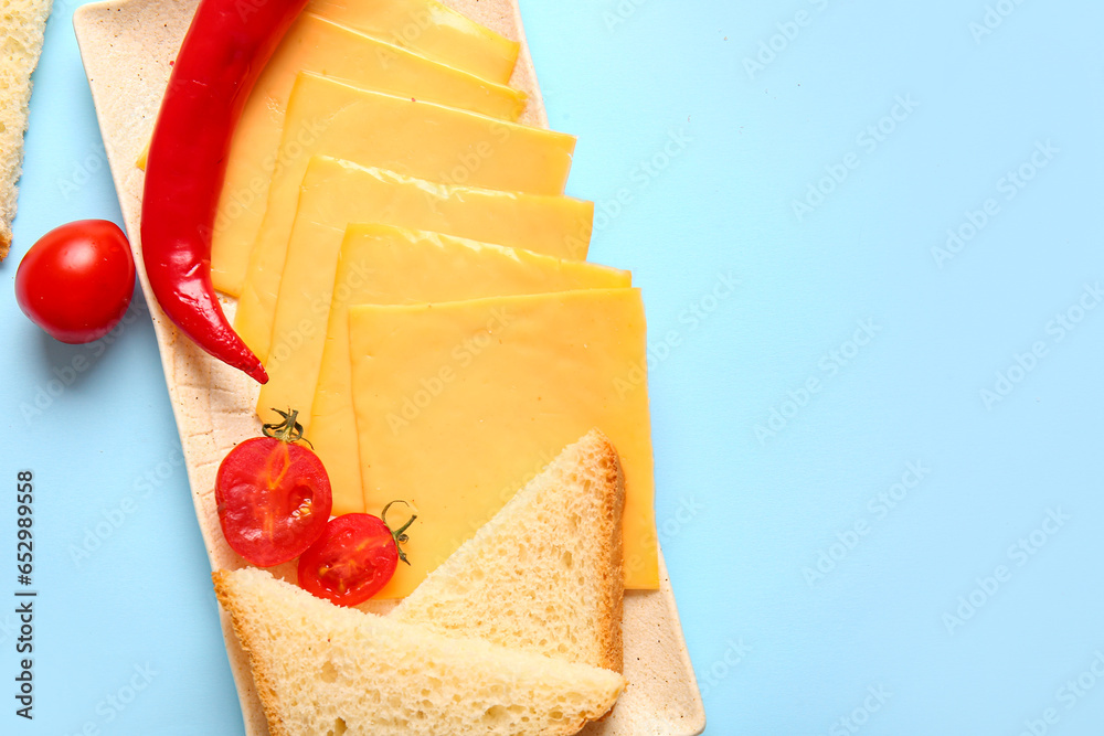 Plate of tasty processed cheese with bread and vegetables on blue background