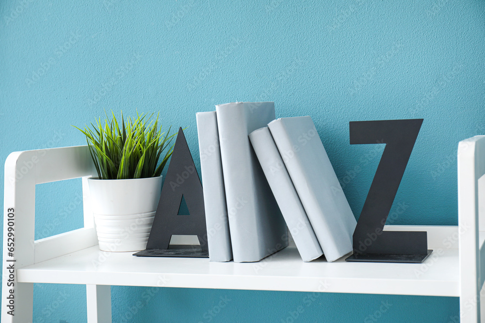 Stylish holder for books with houseplant on shelf near blue wall