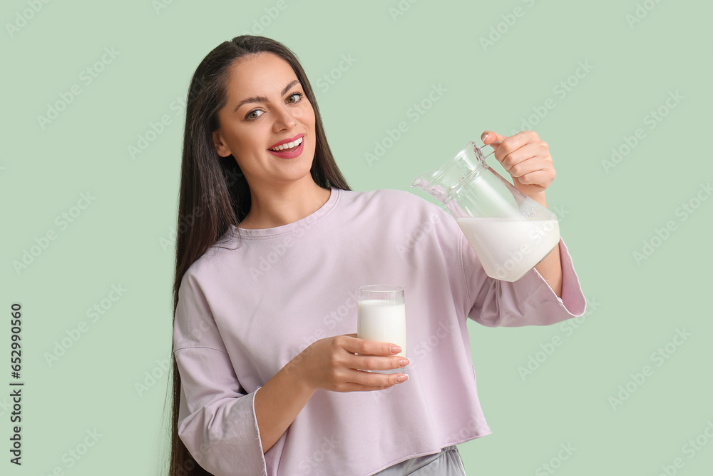 Beautiful young woman with glass and jug of milk on mint background