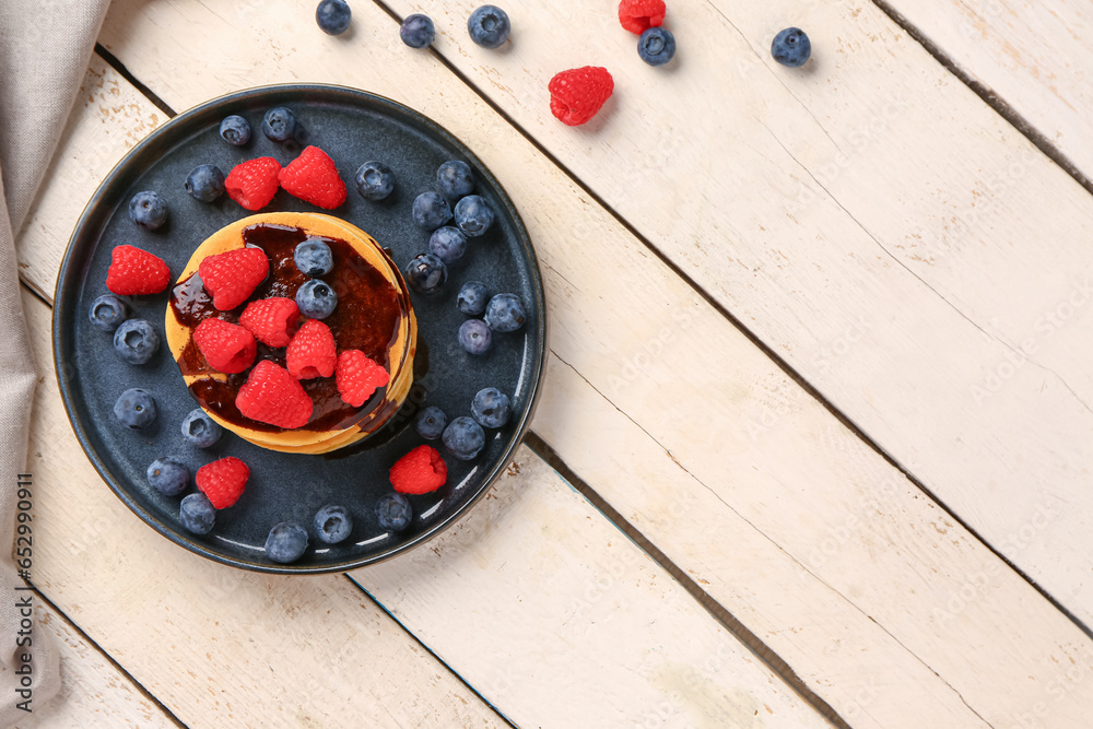 Plate with sweet pancakes and berries on light wooden background