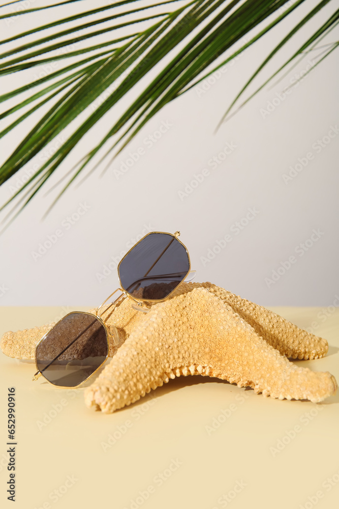 Stylish sunglasses with starfish and palm leaf on light table