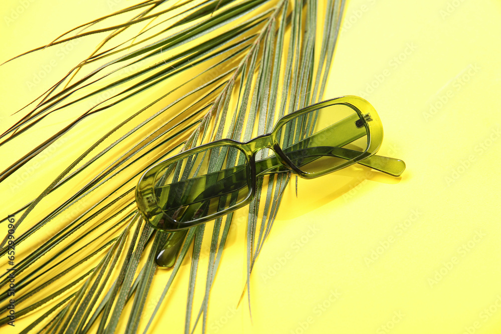 Stylish sunglasses with palm leaf on yellow background