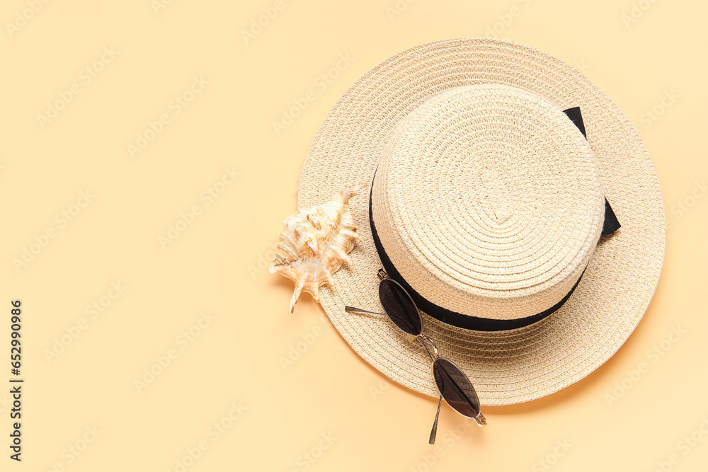 Stylish sunglasses with hat and seashell on beige background