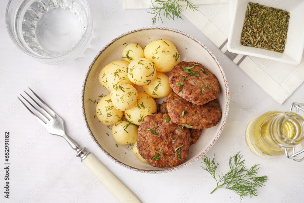 Bowl with cutlets, boiled baby potatoes and dill on white table in kitchen