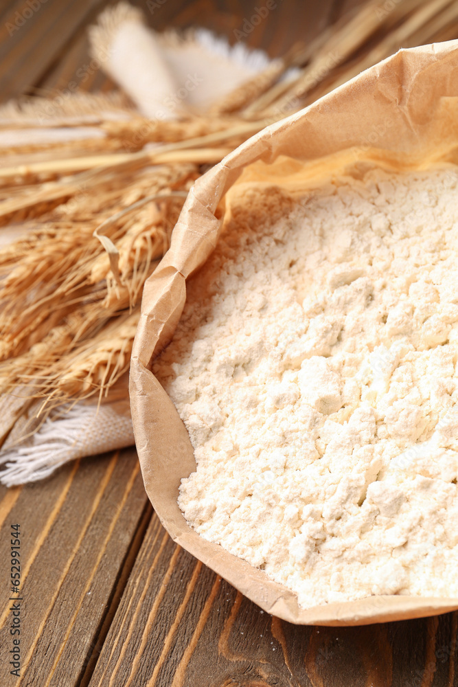 Paper bag with flour and wheat ears on brown wooden background