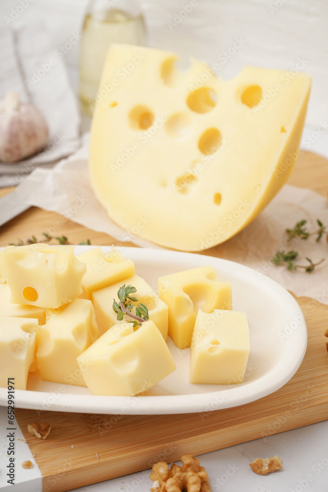 Board and plate with pieces of Swiss cheese on white table