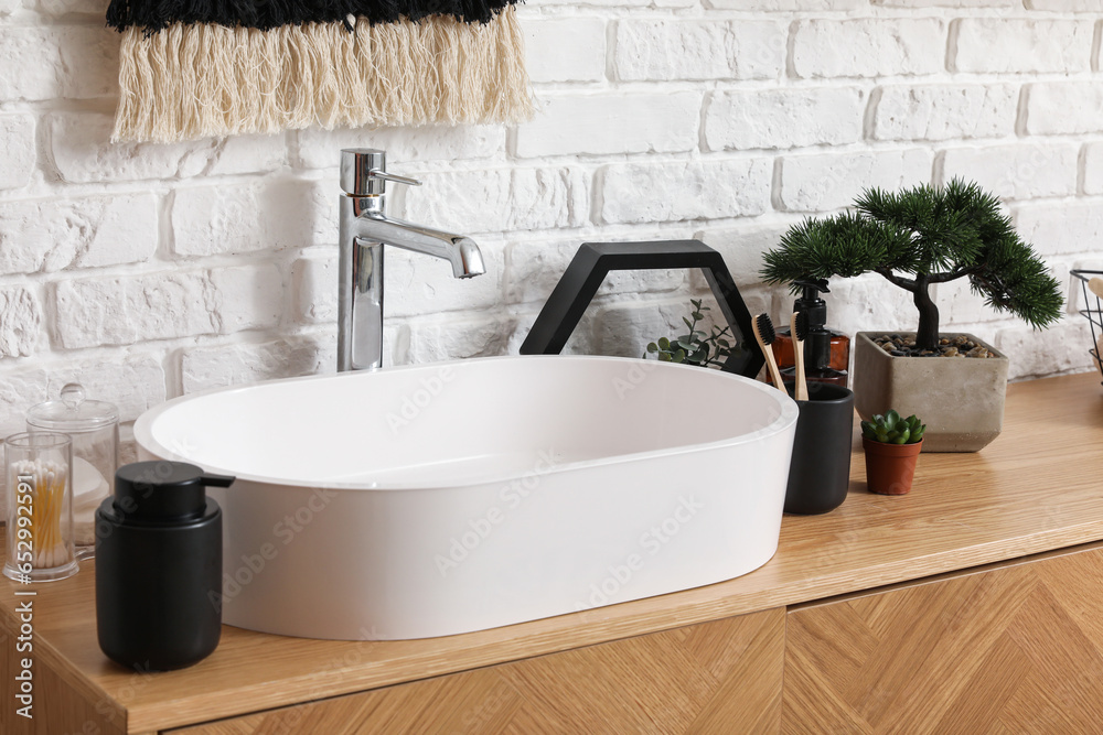 Sink bowl, bath accessories and bonsai tree on wooden cabinet in bathroom