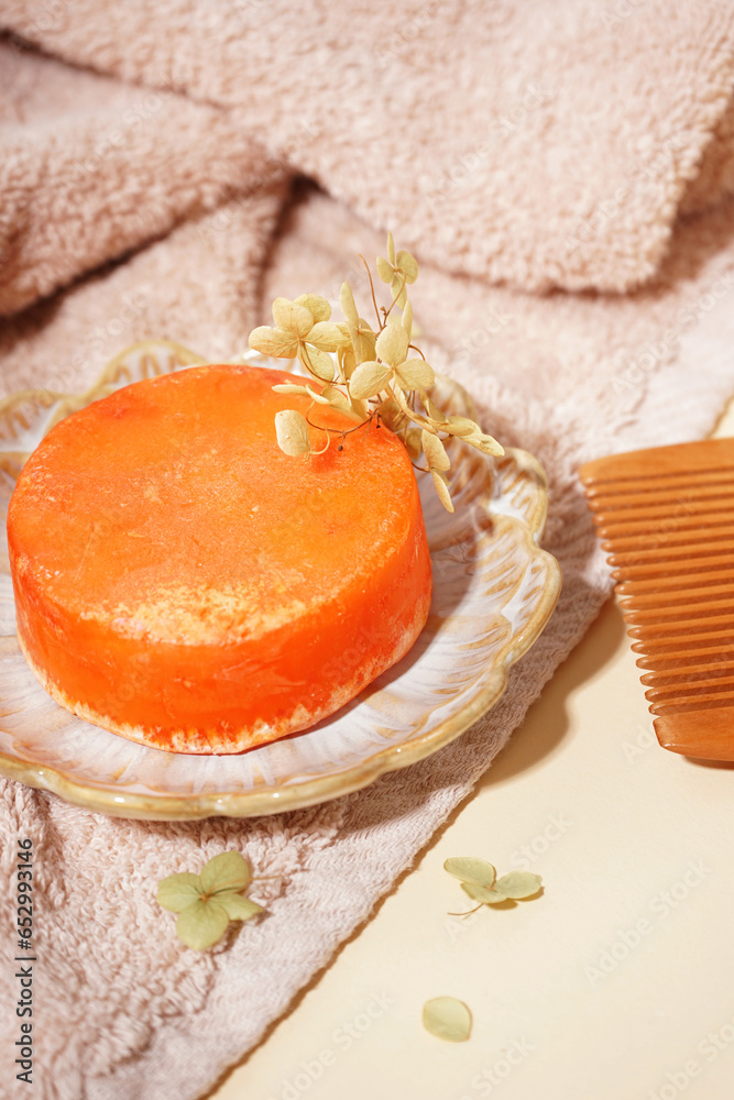 Plate with orange solid shampoo bar, dry lilac and comb on beige background