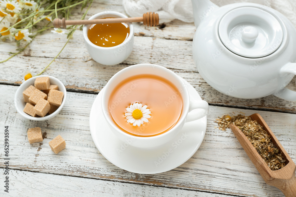 Cup of hot chamomile tea on light wooden background