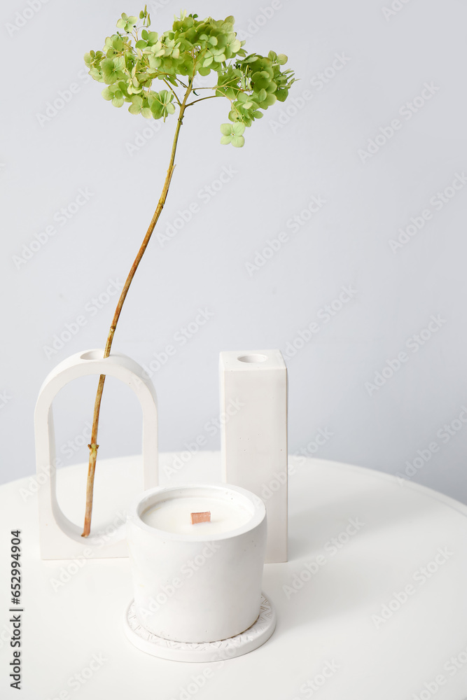 Hydrangea flowers and candle on table near light wall in room, closeup