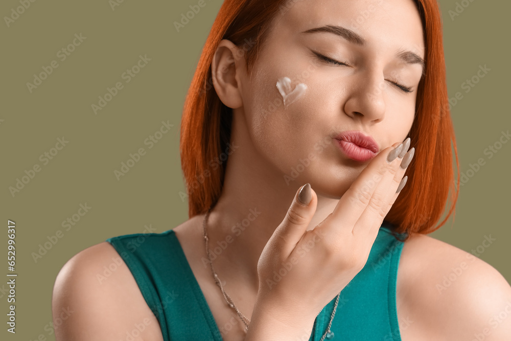 Young woman with heart made of sunscreen cream blowing kiss on green background, closeup