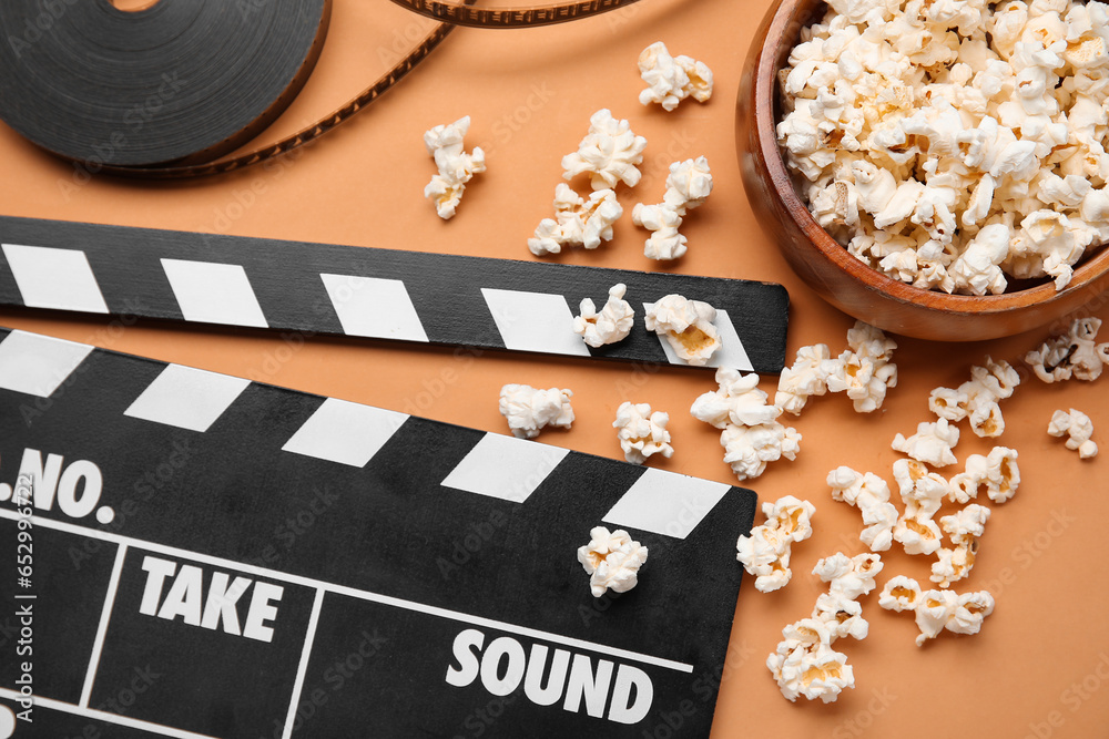 Bowl with tasty popcorn, clapperboard and film reel on brown background