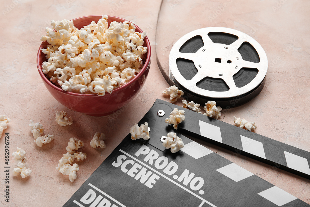 Bowl with tasty popcorn, clapperboard and film reel on light background