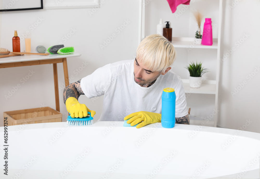 Young tattooed man cleaning bathtub in bathroom