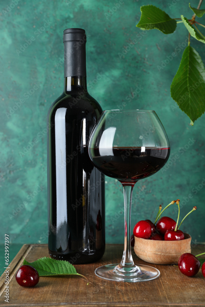 Glass and bottle of sweet cherry liqueur with berries on wooden board near green wall