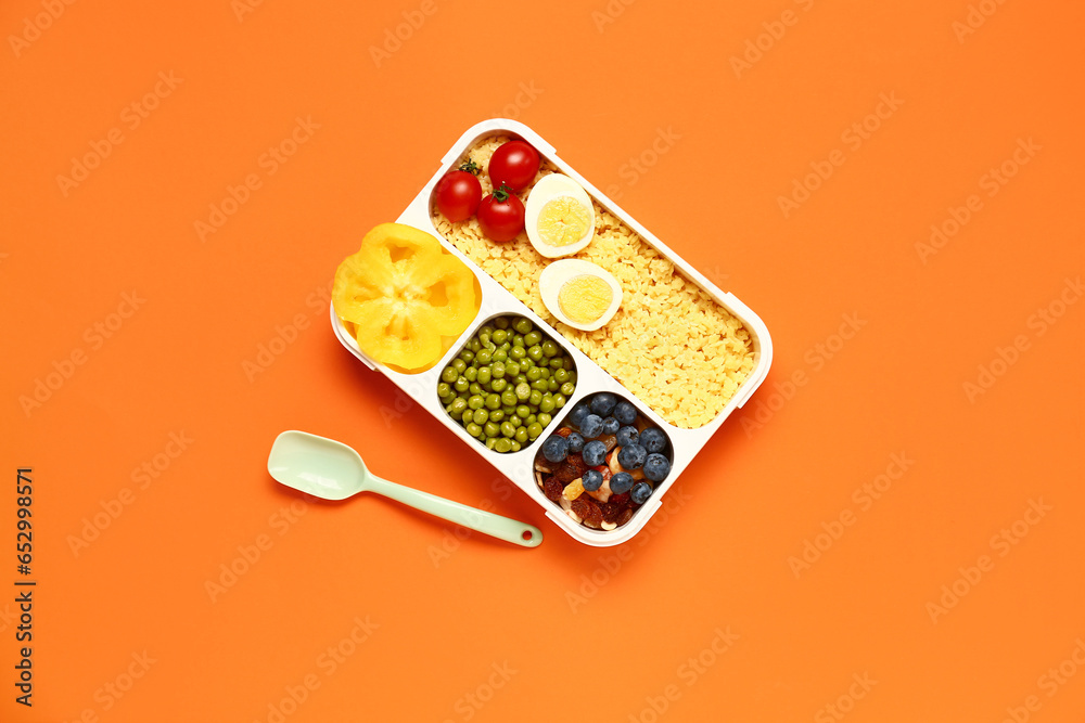 Spoon and lunchbox with tasty food on orange background