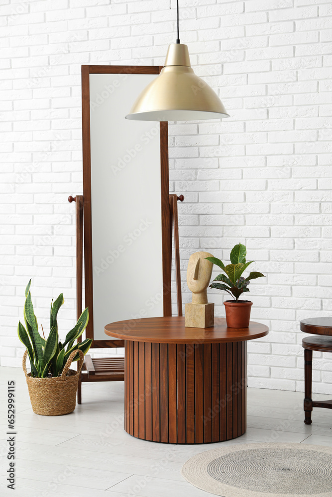 Brown wooden coffee tables with floor mirror and houseplants near white brick wall