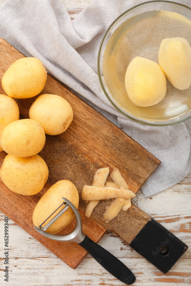 Board and bowl with raw potatoes on white wooden background