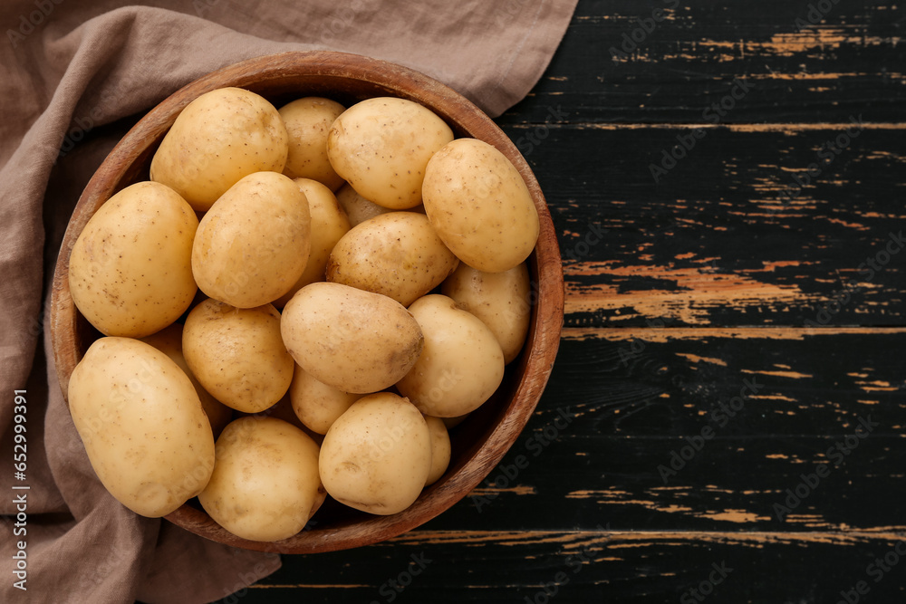 Bowl with raw potatoes on black wooden background