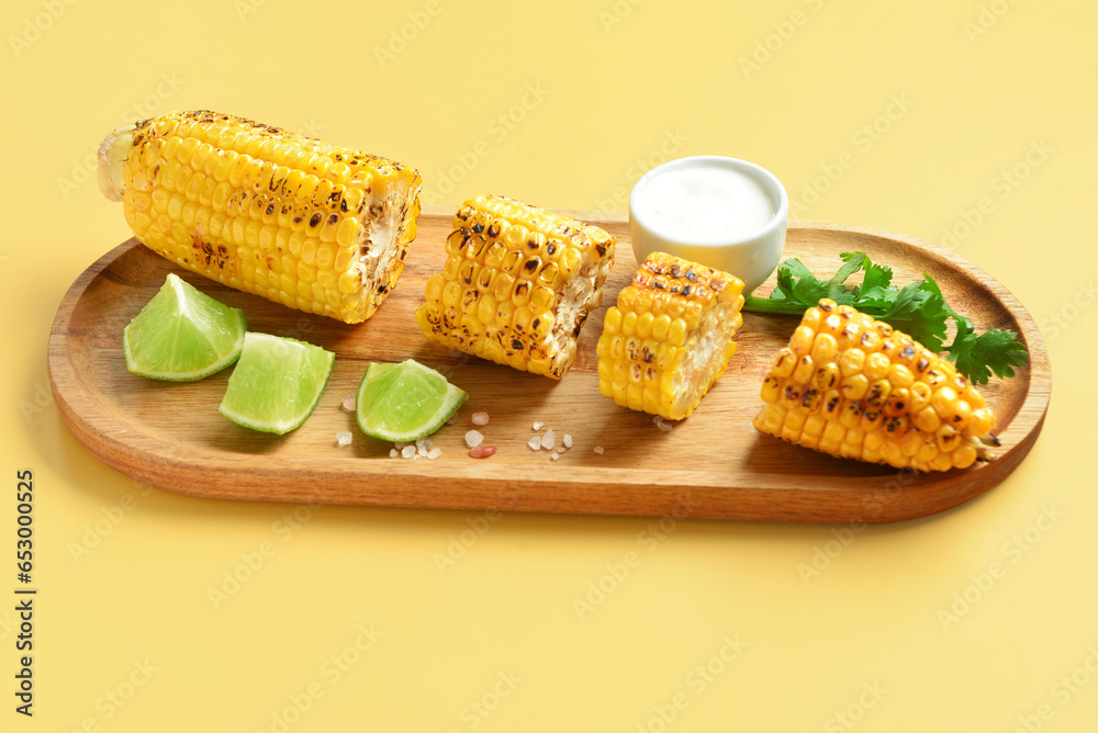 Wooden board with cut tasty grilled corn cob and sauce on yellow background