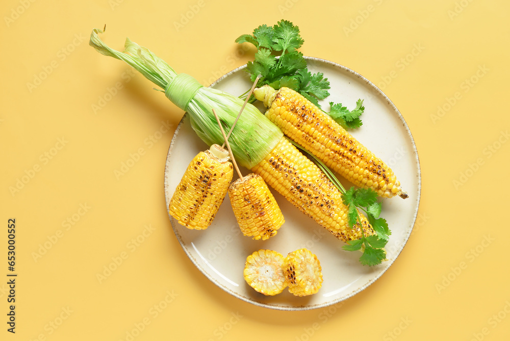 Plate with tasty grilled corn cobs and parsley on yellow background