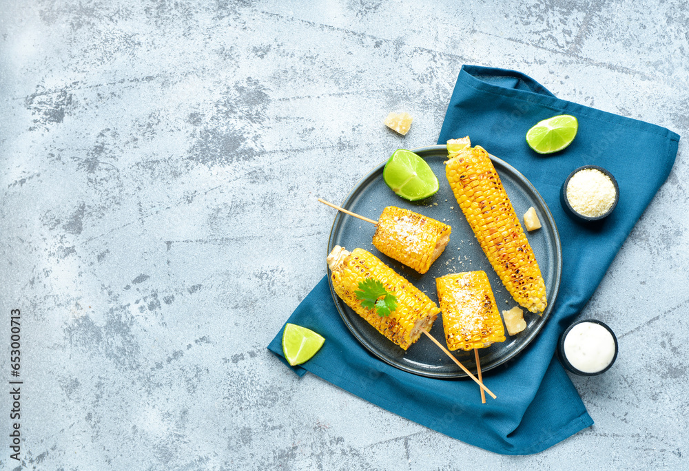 Plate with tasty grilled corn cob skewers and cheese on blue background