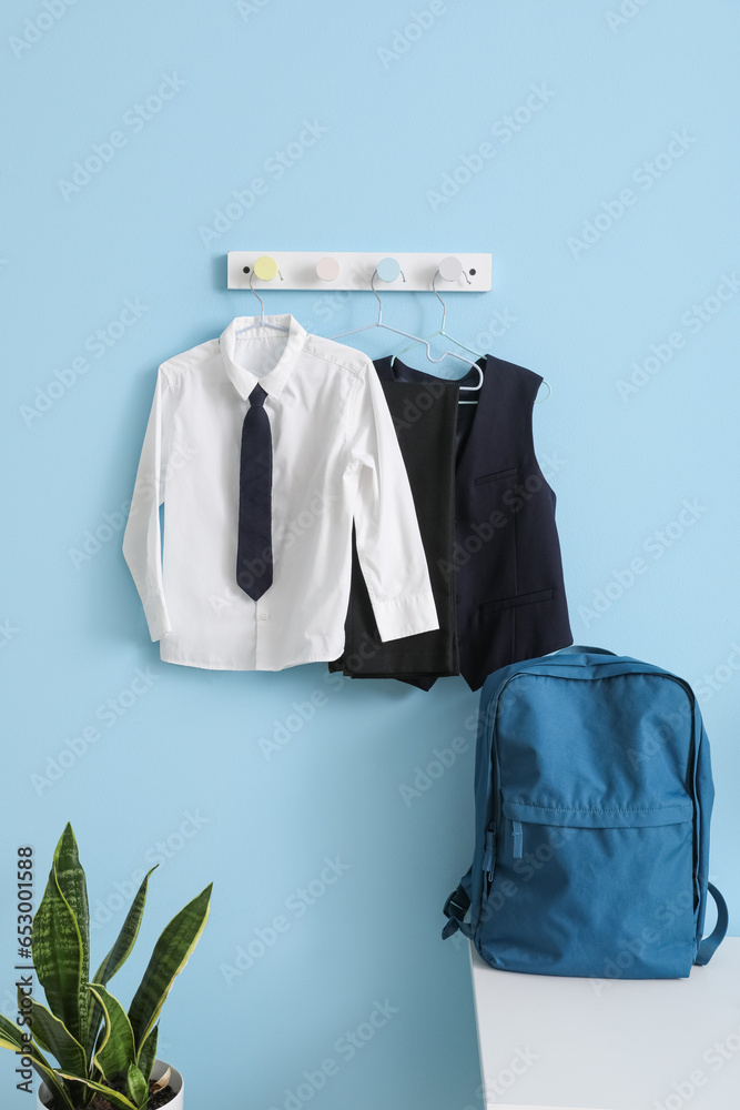 Stylish backpack and school uniform hanging on blue wall in room