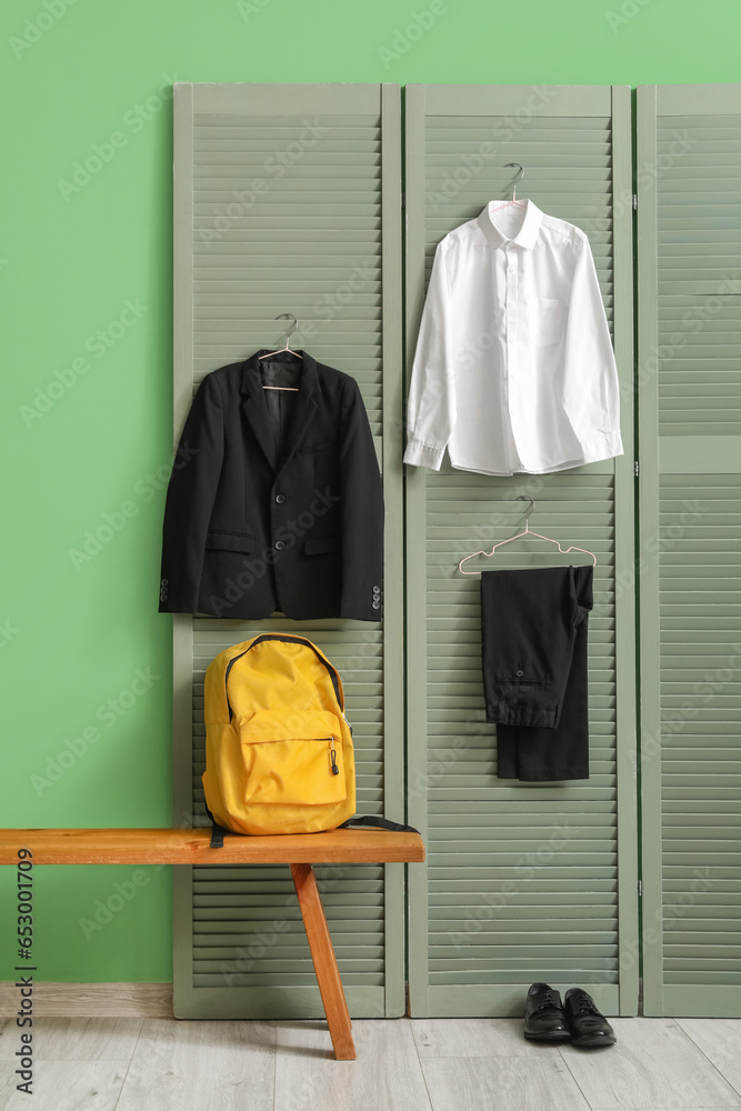 Bench with backpack, shoes and stylish school uniform hanging on folding screen in room