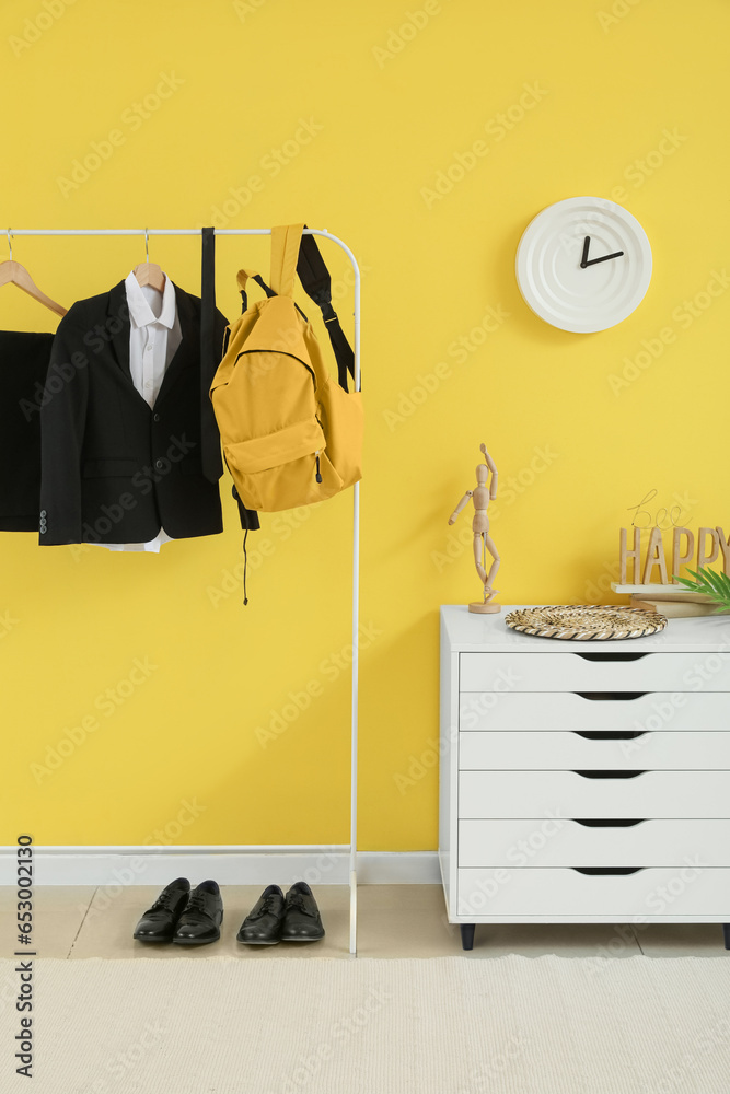 Rack with stylish school uniform and backpack near yellow wall in room