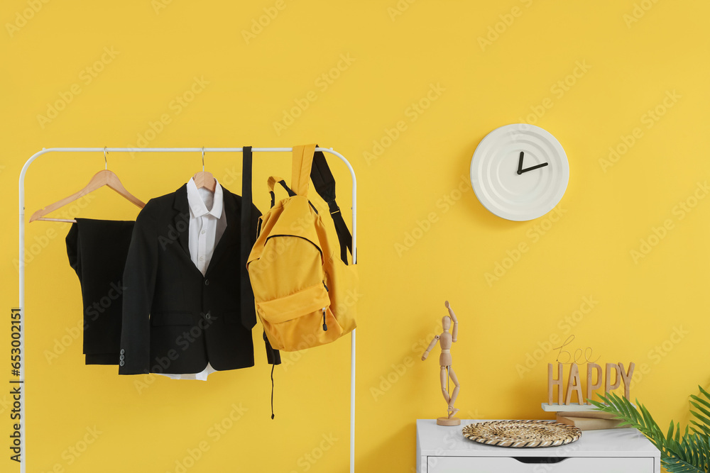 Rack with stylish school uniform and backpack near yellow wall in room