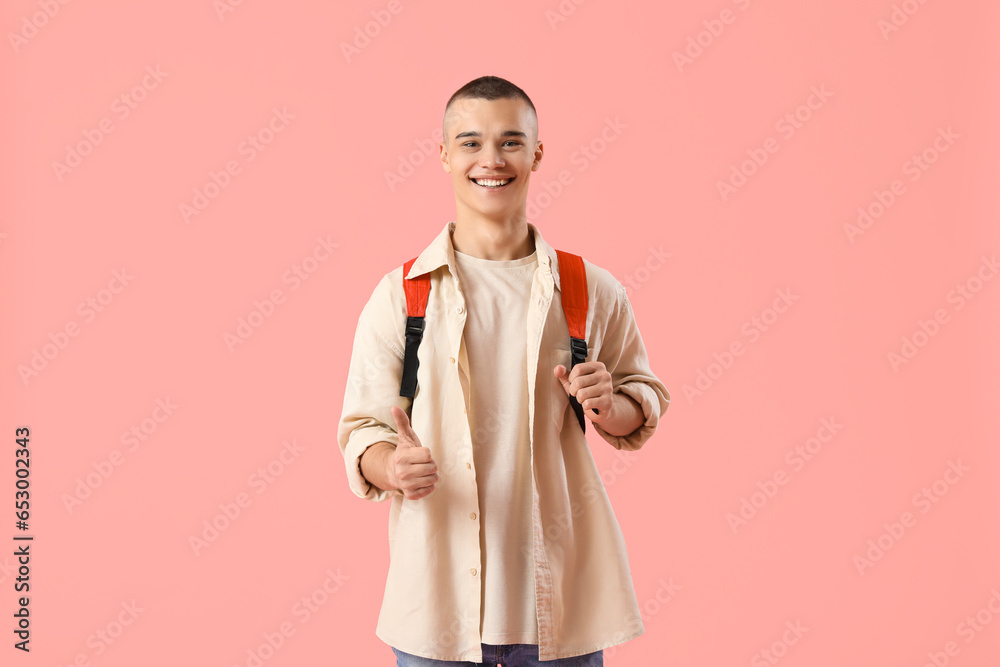 Happy male student with backpack showing thumb-up gesture on pink background