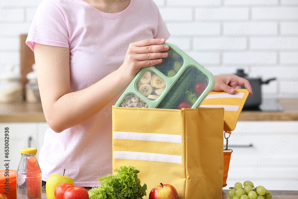 Woman packing fresh meal into lunch box bag in kitchen