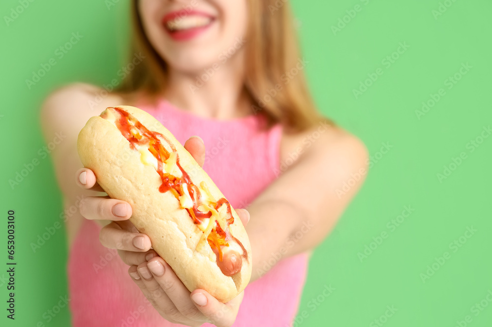 Pretty young woman with tasty hot dog on green background, closeup