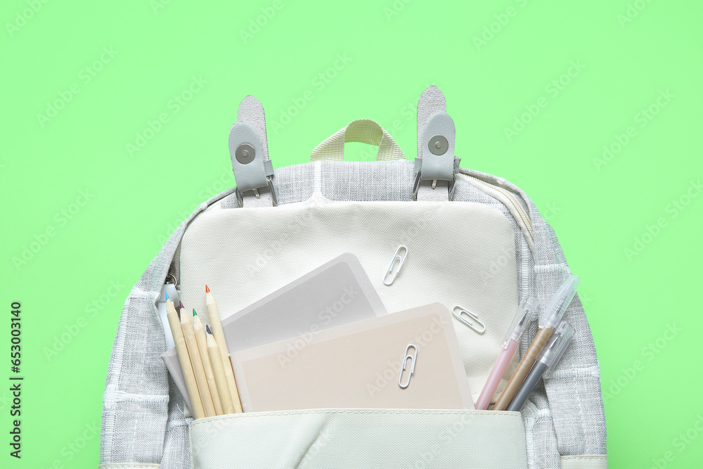 Grey school backpack with different stationery on green background