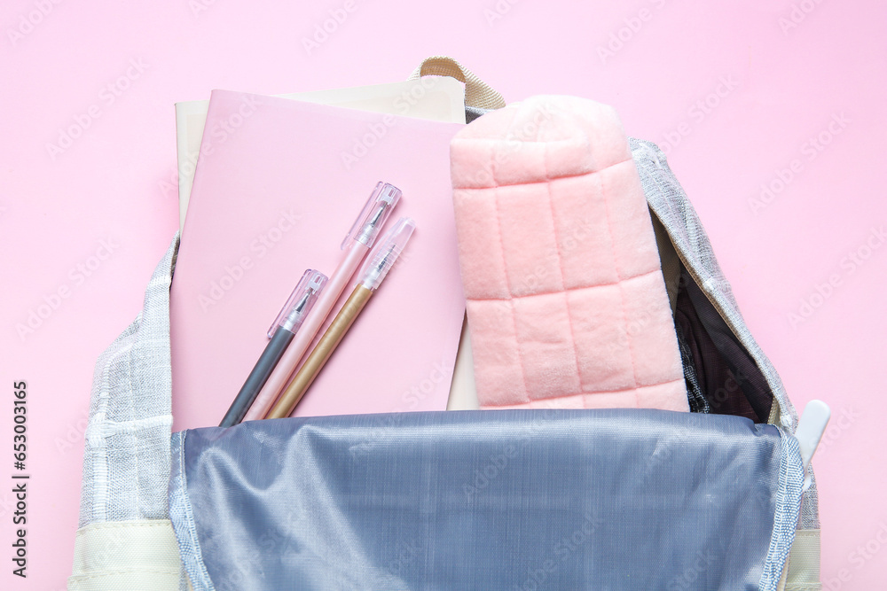 Color school backpack with different stationery on pink background