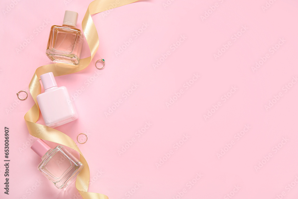 Perfume bottles, rings and golden ribbon on pink background