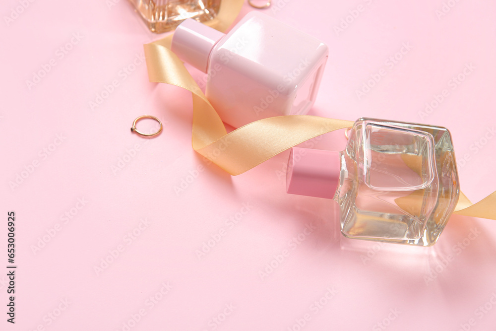 Perfume bottles, rings and golden ribbon on pink background