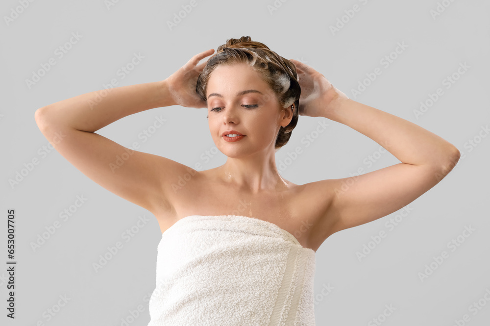 Young woman washing hair on light background